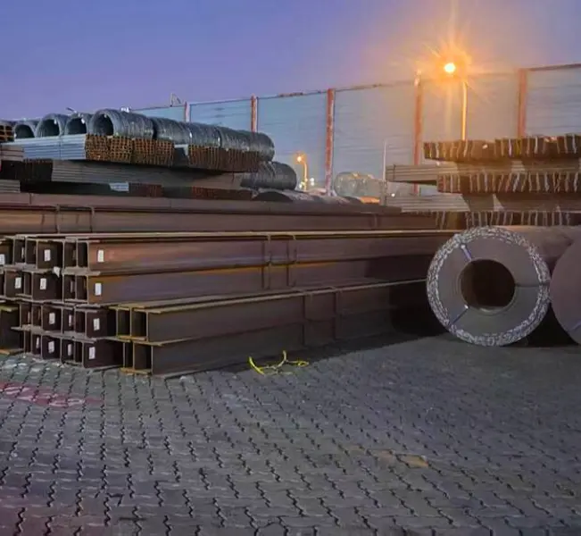 H beam structural steel profiles stored alongside steel coils at an industrial warehouse yard